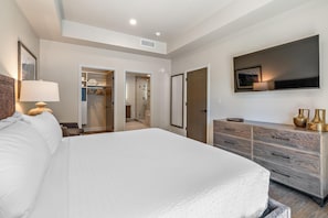 Ein modernes Hotelzimmer mit einem großen Bett, einem Schminktisch, einem Fernseher und einem begehbaren Kleiderschrank.