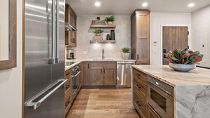 A modern kitchen with stainless steel appliances, wooden cabinets, and a marble countertop. - Suite Serenity | Includes Two 1-Day Lift Tickets (Tamarack)