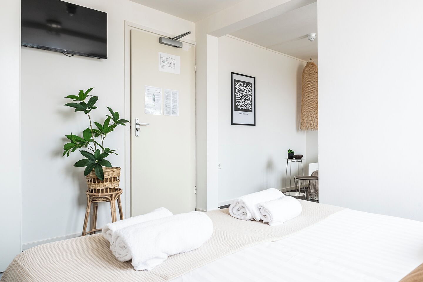 Ein Hotelzimmer mit zwei Betten, einem Fernseher, einer Tür mit Papieren, einer Pflanze und einem Wandbild.