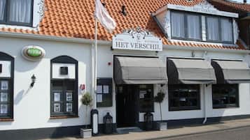 Een wit gebouw met een betegeld dak, een bord waarop staat 'HET VERSCHIL HOTEL RESTAURANT', en een vlag.