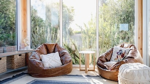 Een moderne woonkamer met twee leren loungestoelen, een klein rond tafeltje en een groot raam met uitzicht op groen.