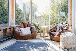 Relax in a serene space with a view of lush greenery, featuring a comfortable seating area with a wooden bench and woven storage.