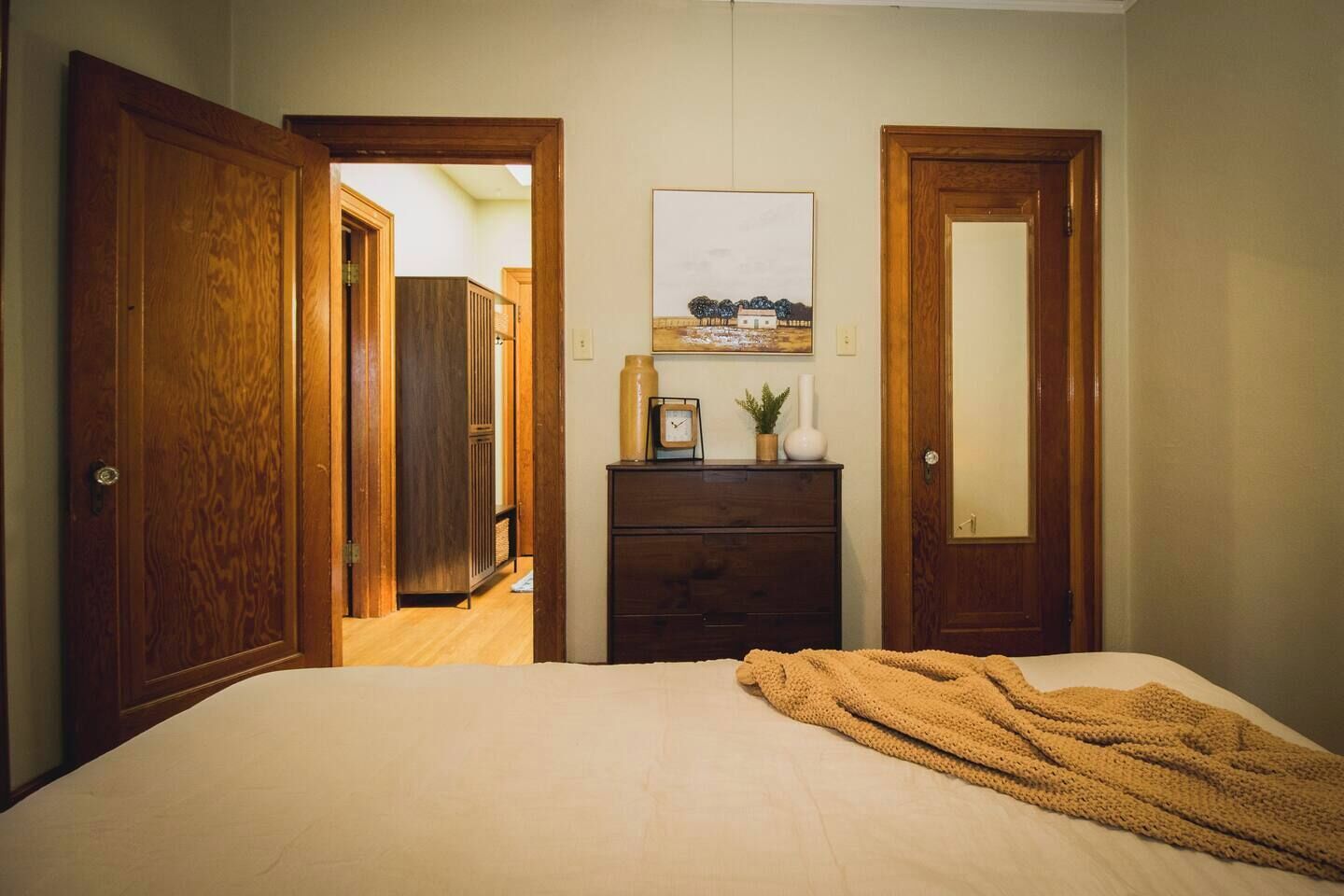 Een slaapkamer met een bed, een dressoir en een schilderij aan de muur.