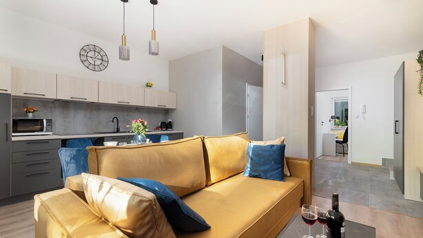 Un salon moderne avec un canapé, une table à manger agrémentée d’une bouteille de vin, et une cuisine en arrière-plan.