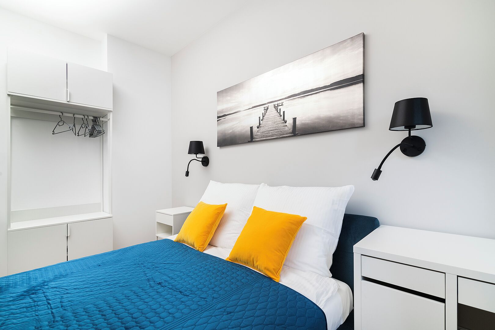 Una camera da letto moderna con un letto, un'armadio bianco e un quadro appeso al muro.