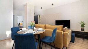Un salon moderne comprenant un canapé, une table à manger avec des chaises, un téléviseur à écran plat et une plante en pot.