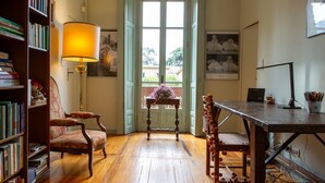 A room with a wooden floor, a table, a chair, a bookshelf, a lamp, and a window with a view of the outside. - Villa Nanni offers the perfect balance between privacy and convenience, allowing you to easily explore everything Cernobbio has to offer. The villa is reminiscent of 19th-century chalets and stands out for the distinctive decoration of the f (Cernobbio)