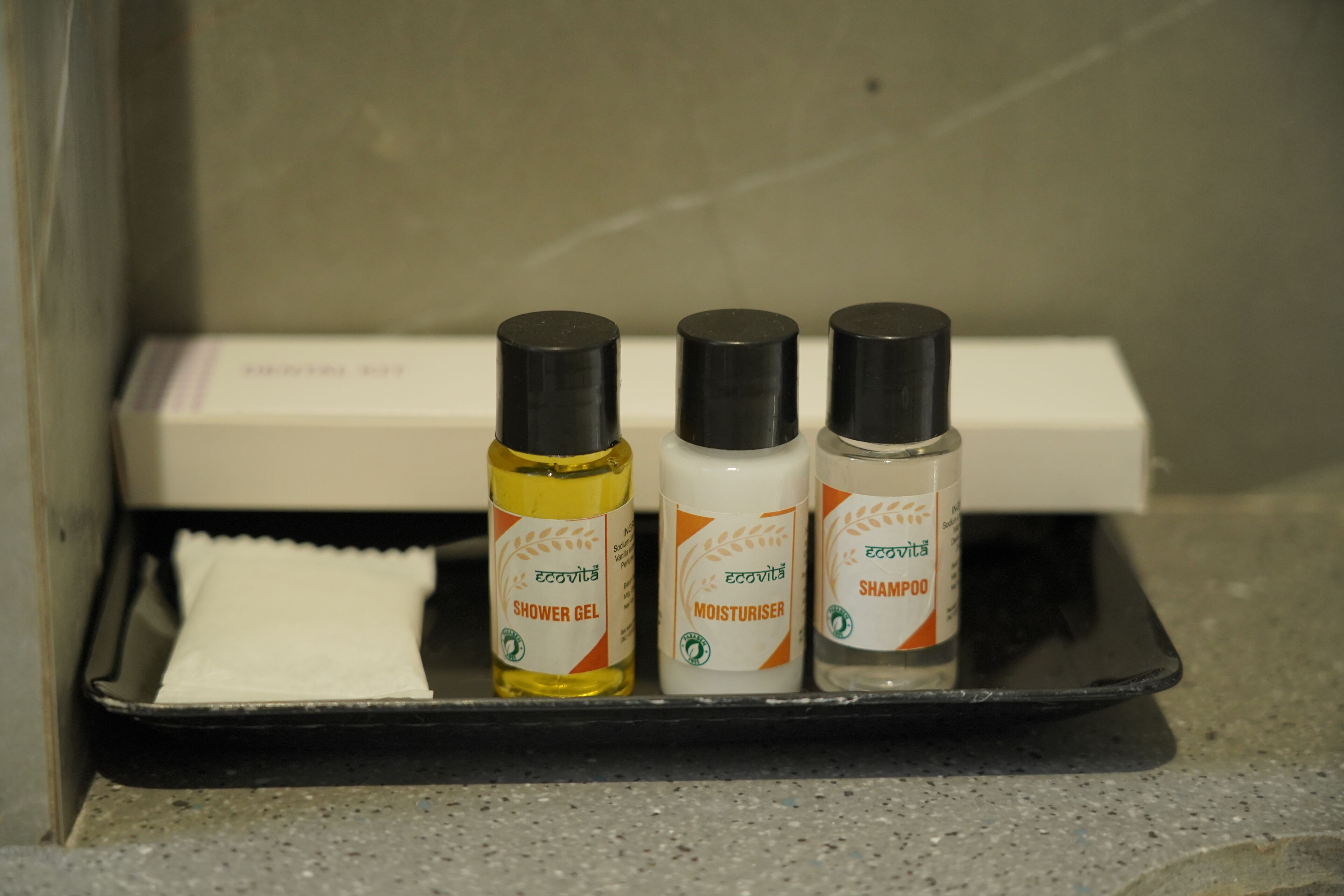 A bathroom shelf with three bottles of shower gel, a bottle of moisturizer, and a white towel.