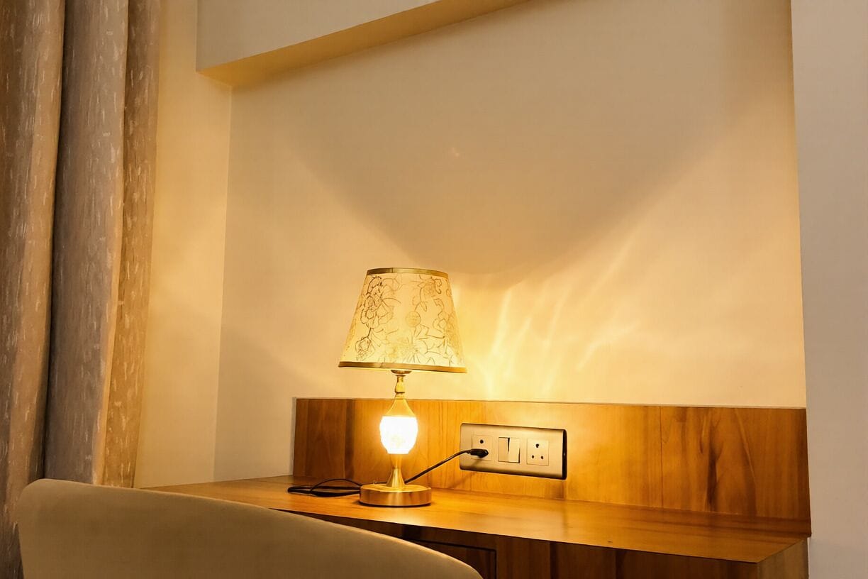 A bedside table with a lamp, a power outlet, and a wooden panel on the wall.