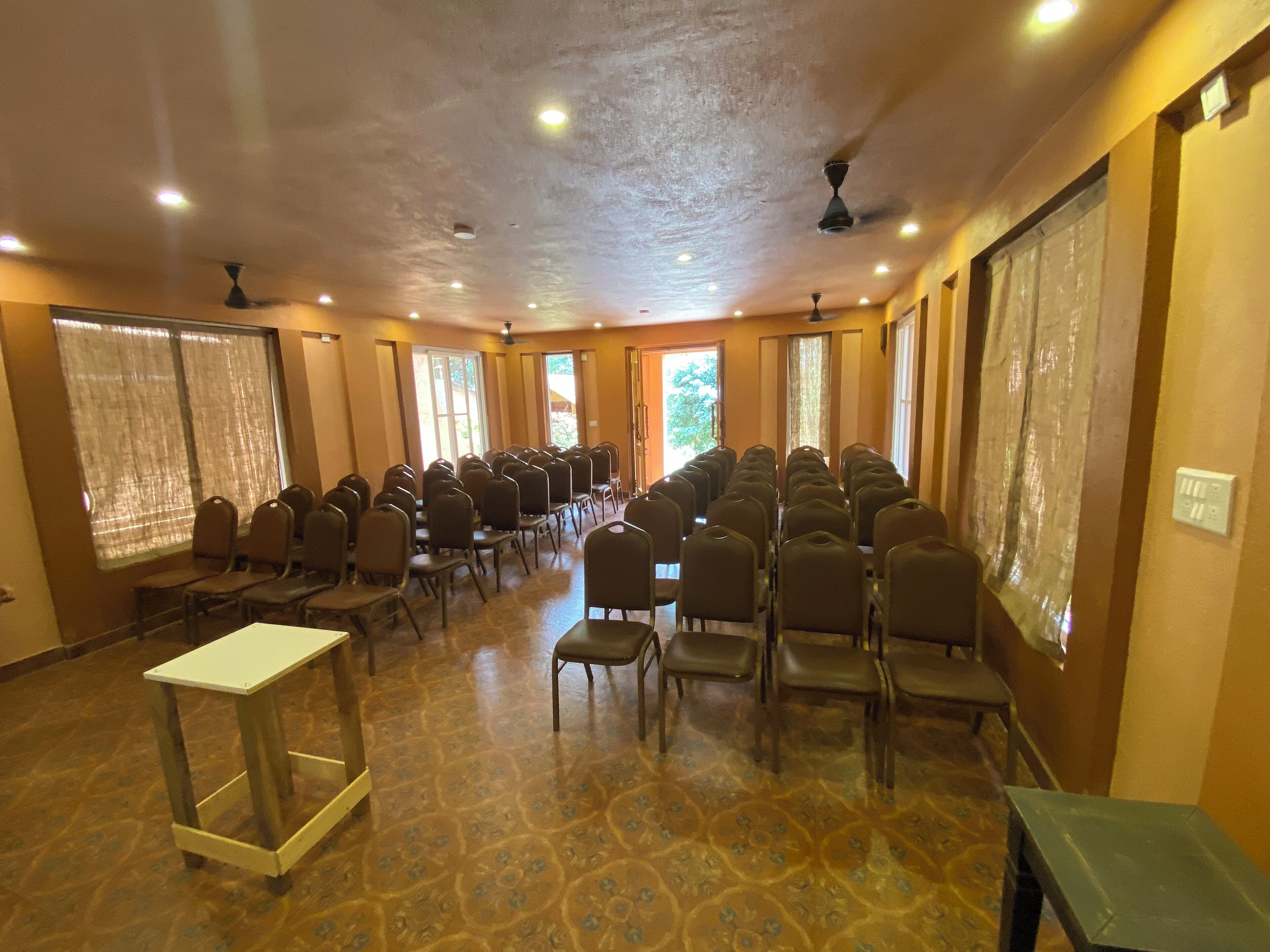 A conference room with rows of chairs, a white table, and ceiling fans.