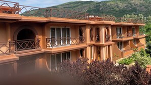 Un edificio de varios pisos con balcones, ventanas de arco y vista a un paisaje montañoso.