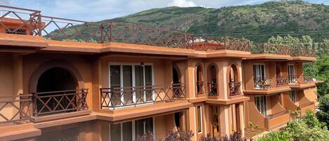 A multi-story building with balconies, arched windows, and a view of a mountainous landscape.