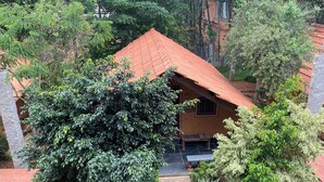 Un edificio rústico con techo rojo, rodeado de vegetación exuberante y un sendero de piedra que lleva a un banco de madera.