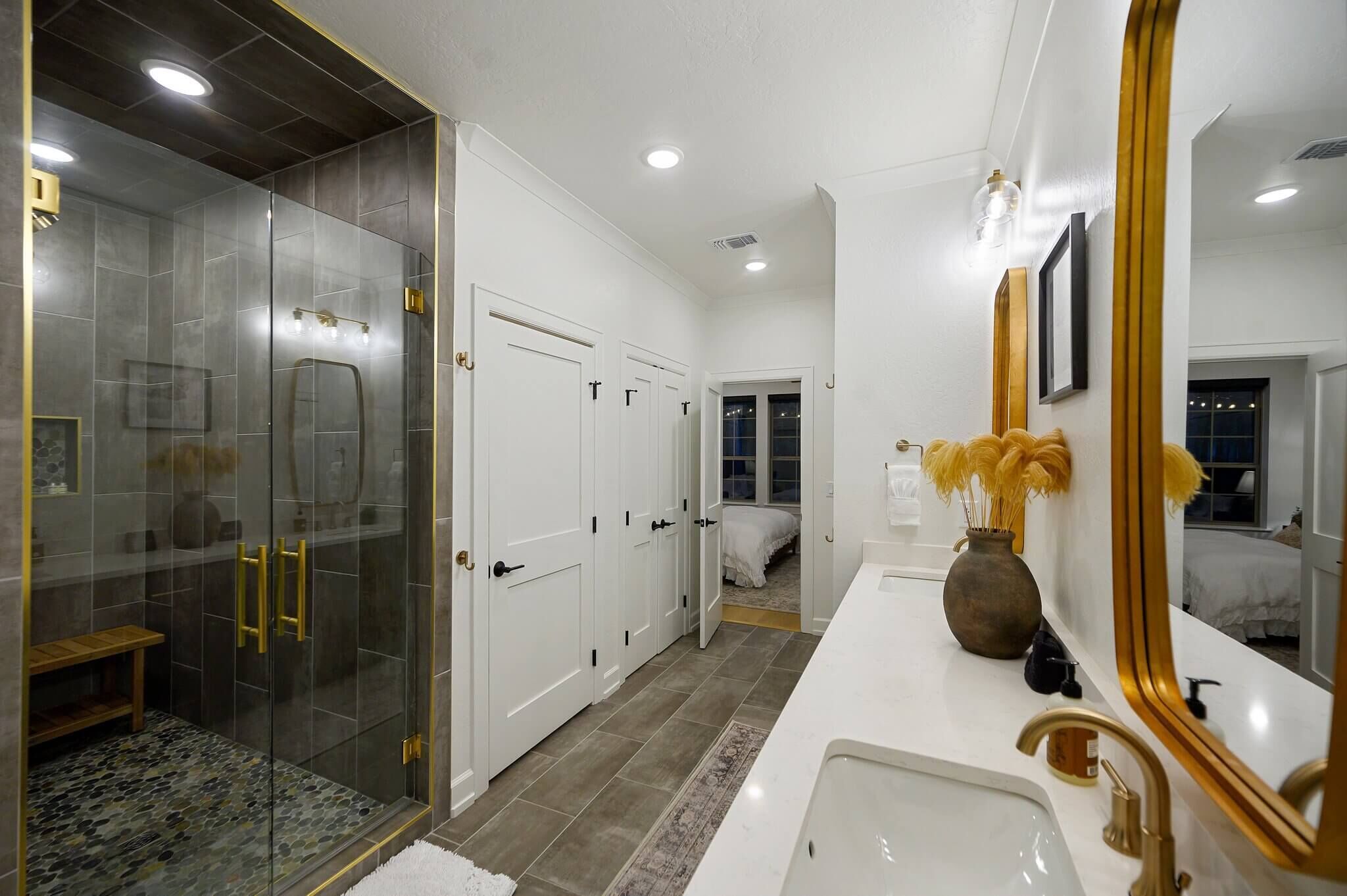 Une salle de bain moderne avec une douche à parois de verre, un meuble-lavabo blanc doté de robinetterie dorée et un grand miroir.