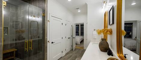 A modern bathroom with a glass-enclosed shower, white vanity with gold fixtures, and a large mirror.