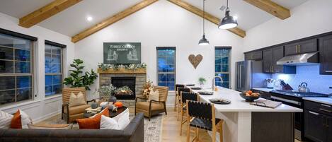 Un salón comedor espacioso con chimenea, zona de comedor y cocina con armarios oscuros y electrodomésticos modernos.