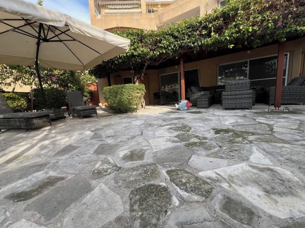 Un patio con suelo de piedra, mobiliario exterior y una zona cubierta con una sombrilla blanca.