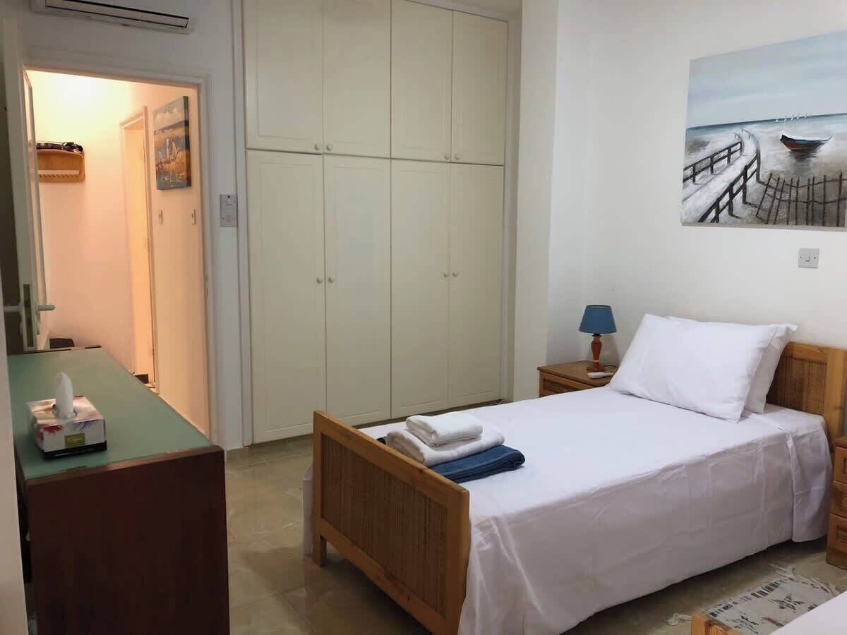 A bedroom with a bed, a nightstand, a desk, a wardrobe, and a painting on the wall.