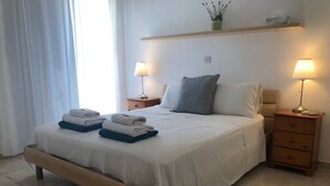 A neatly made bed with towels, a bedside lamp, and a nightstand with a plant.