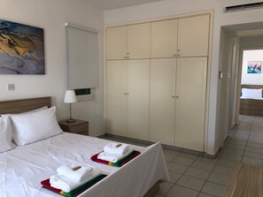 Una habitación de hotel con cama, armario, mesita de noche, lámpara y un cuadro en la pared.
