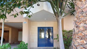 A building entrance with a blue door, a stone pathway, and a small garden area with plants. - Kings Palace: Large 2BR Apt | Opp. Beach | Pool (Paphos)