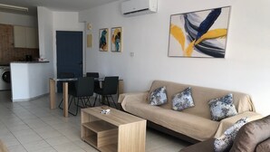 A modern living room with a sofa, coffee table, and dining area. - Kings Palace: Large 2BR Apt | Opp. Beach | Pool (Paphos)