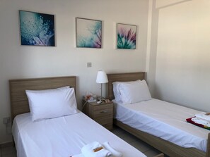 Una habitación de hotel con dos camas, una mesita de noche con lámpara y tres obras de arte colgadas en la pared.