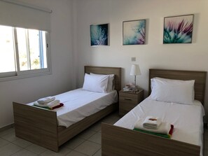 A hotel room with two beds, a window, and artwork on the wall. - Kings Palace: Large 2BR Apt | Opp. Beach | Pool (Paphos)