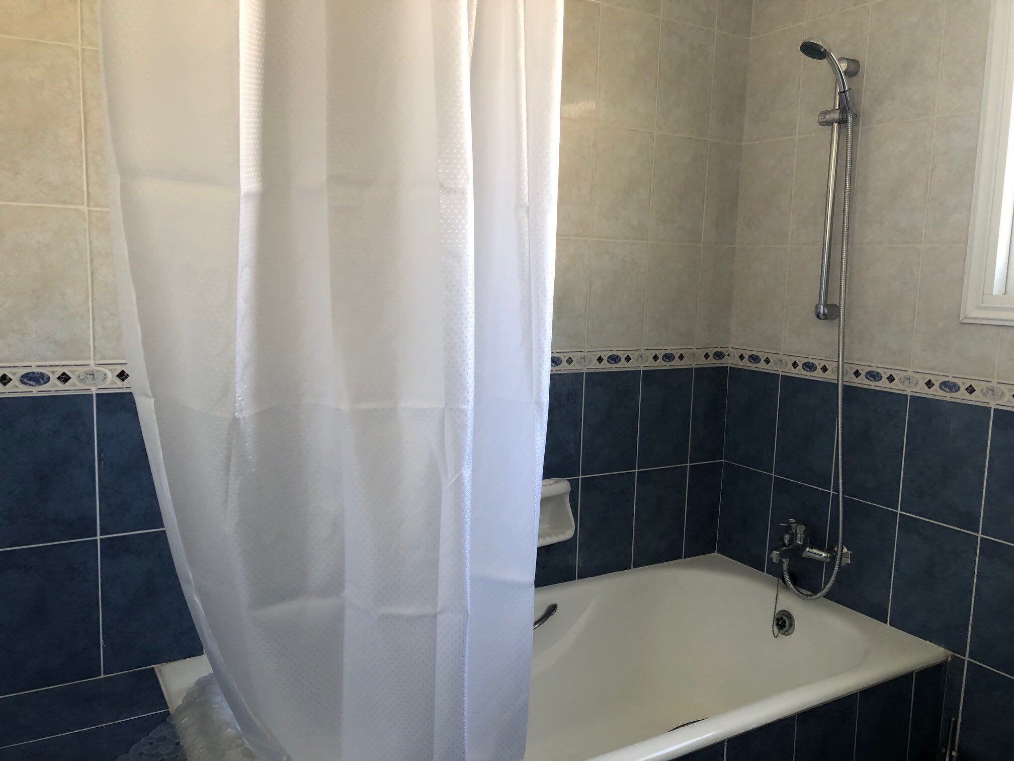 A bathroom with a shower, a bathtub, and a white curtain.