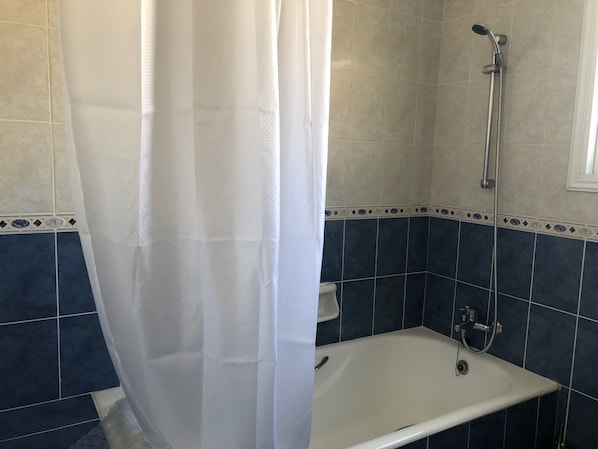 A bathroom with a shower, a bathtub, and a white curtain.