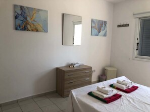 Une chambre d’hôtel avec un lit, une commode en bois, un miroir et des œuvres d’art abstraites accrochées au mur.