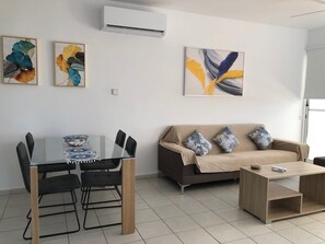 A modern living room with a glass dining table, black chairs, a brown sofa with patterned cushions, and a wooden coffee table.