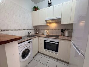 A compact kitchen with a washing machine, an oven, and a sink. - Limnaria: Modern 1 Bed, Pool Views, 5min To Beach (Paphos)