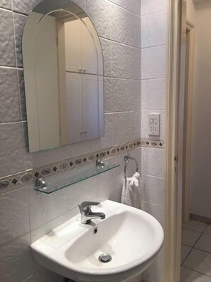 A bathroom with a white sink, a mirror, and a glass shelf. - Limnaria: Modern 1 Bed, Pool Views, 5min To Beach (Paphos)