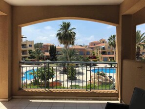 A balcony with a view of a swimming pool, palm trees, and residential buildings. - Limnaria: Modern 1 Bed, Pool Views, 5min To Beach (Paphos)