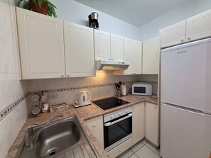 Eine kleine Küche mit weißen Schränken, einer eingebauten Mikrowelle, einem Herd und einem Kühlschrank.