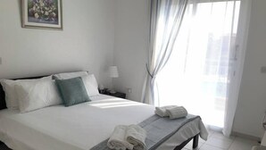 Una habitación de hotel con una cama bien hecha, una lámpara de noche y una ventana con cortinas.