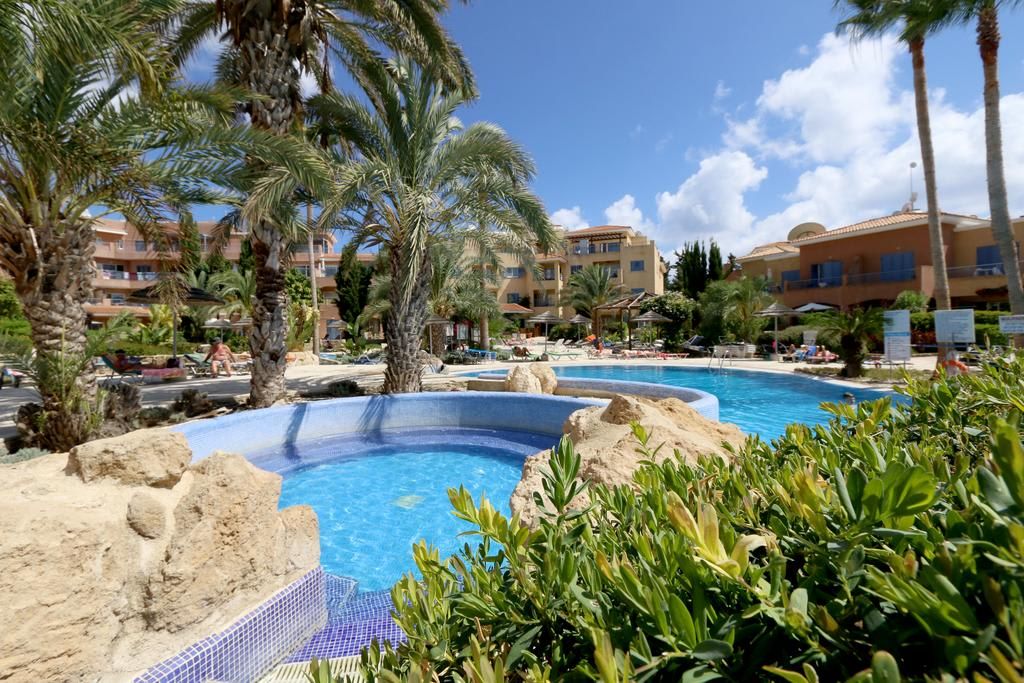 Una piscina de resort rodeada de palmeras y un edificio con varios balcones.