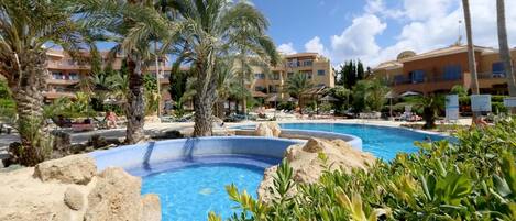 Una piscina de resort rodeada de palmeras y un edificio con varios balcones.