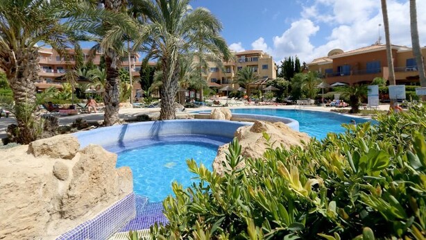Una piscina de resort rodeada de palmeras y un edificio con varios balcones.