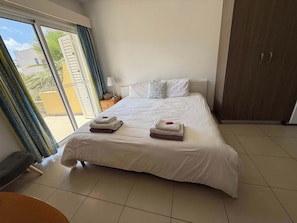 A hotel room with a bed, two towels, a nightstand, a lamp, a wardrobe, and a view of the outside.