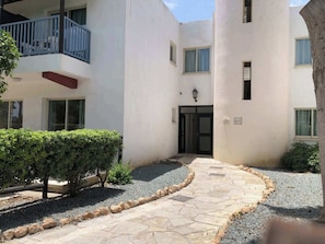 A courtyard with a stone pathway, a small tree, and a building with a balcony.