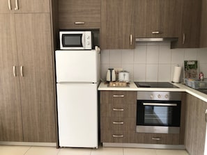 A kitchen with a microwave, refrigerator, toaster, kettle, and oven.