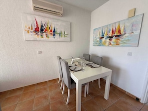 Un comedor con una mesa blanca, sillas grises y dos cuadros en las paredes.
