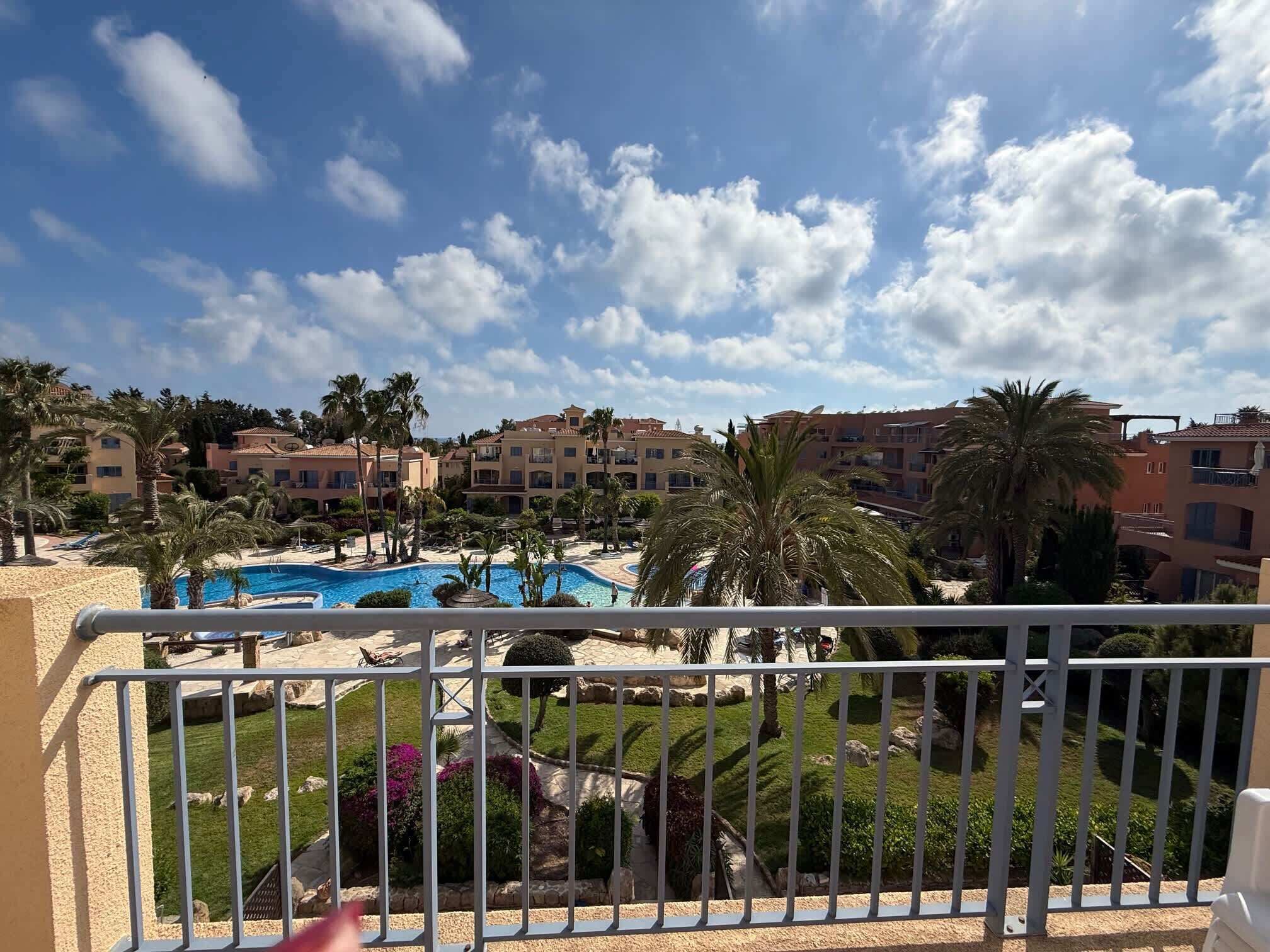 A resort with a swimming pool, palm trees, and Mediterranean-style buildings.