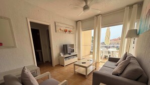 En stue med sofa, fjernsyn, sofabord og en balkon med udendørs møbler.