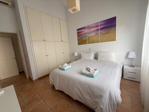 Una habitación de hotel con cama, armario, mesita de noche, lámpara y un cuadro en la pared.