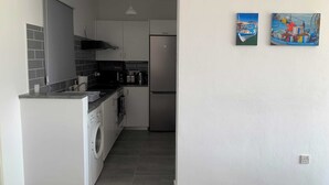 Une cuisine compacte équipée d’un lave-linge, d’un réfrigérateur et d’un four à micro-ondes. Deux tableaux sont accrochés au mur.