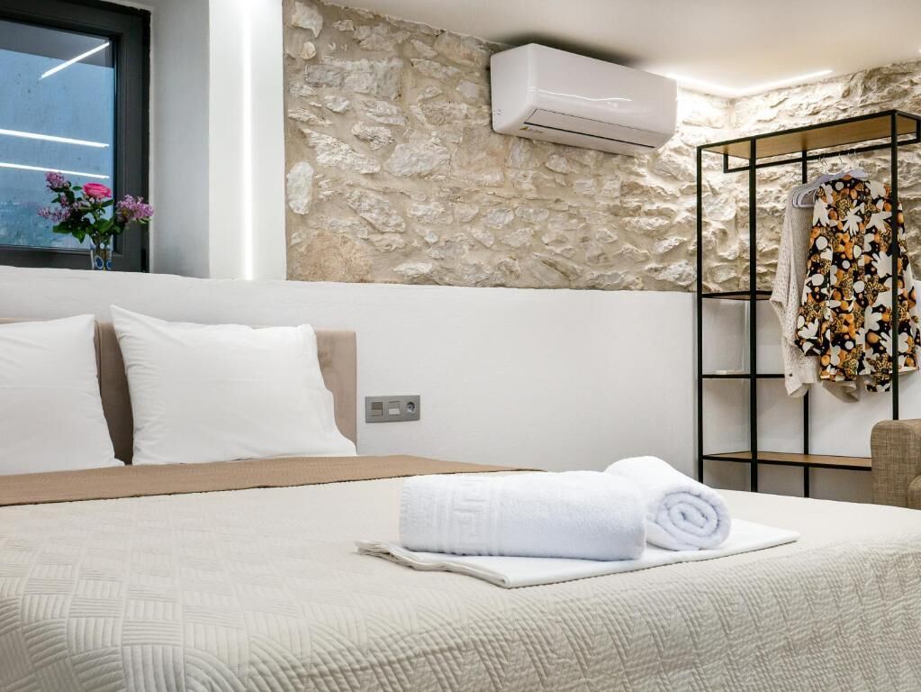 Habitación de hotel con cama, pared de piedra, unidad de aire acondicionado y toallero con toalla floral.