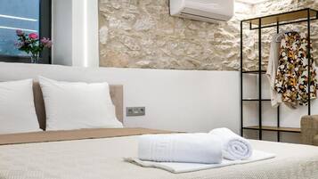 Habitación de hotel con cama, pared de piedra, unidad de aire acondicionado y toallero con toalla floral.